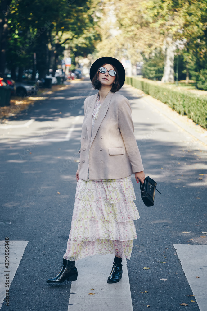 fashion blogger street style. fashionable woman posing wearing an oversized blazer, floral vintage dress, black ankle boots and a black trendy mini handbag. detail of a perfect fall 2019 outfit. 