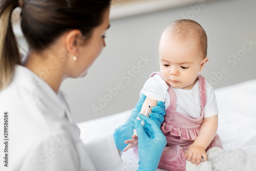 medicine, healthcare and vaccination concept - female pediatrician doctor or nurse with syringe making injection of vaccine for baby girl patient at clinic or hospital