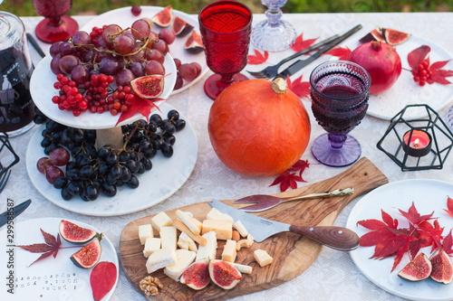 Autumn harvest snack board. Cheese, nuts, pomegranate, pumpkin, sliced figs, red and black grape, berries and glasses of wine on picnic decorated table. 