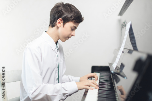 a teenage boy in a white shirt sits and plays the piano . a man plays a musical instrument piano