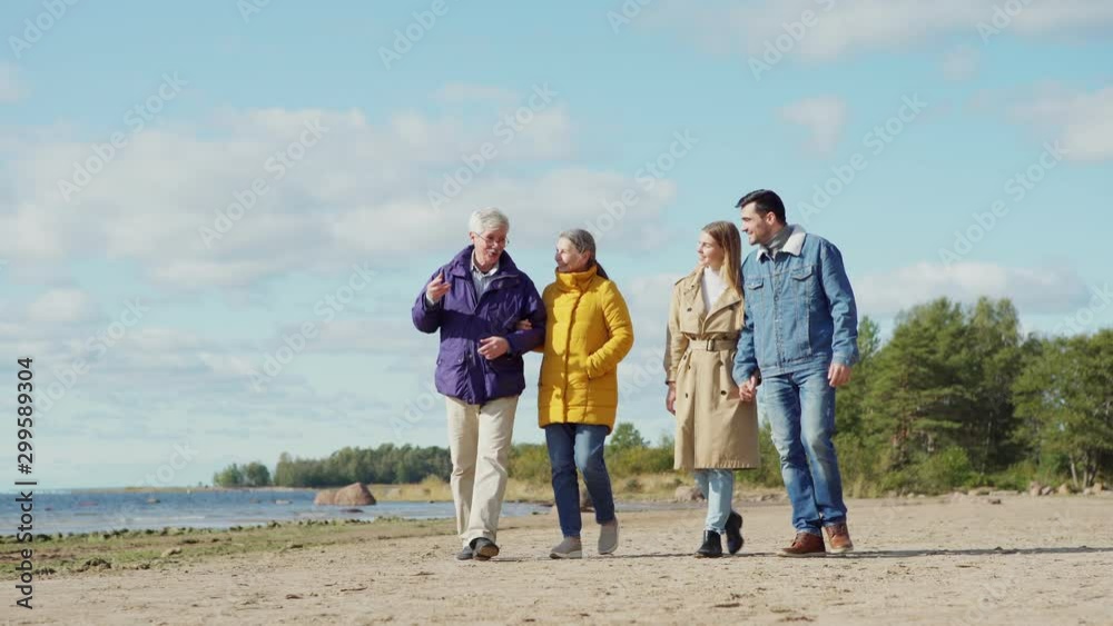 Wide shot of two happy loving couples, senior and young lovers, walking on sea shore together and talking joyfully on spring day Wide shot of two happy loving couples, senior and young lovers, walking on sea shore together and talking joyfully on spring day