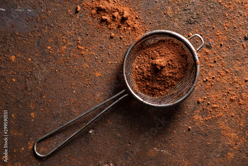 Cocoa powder in sifter on brown, metal background.