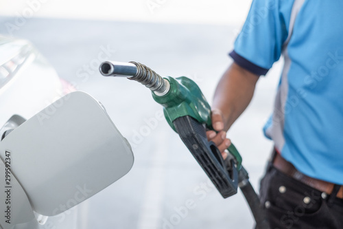 Close up of gasoline hose or nozzle pump held by service man hand at gas station. Energy, fuel, oil, and transport concept.