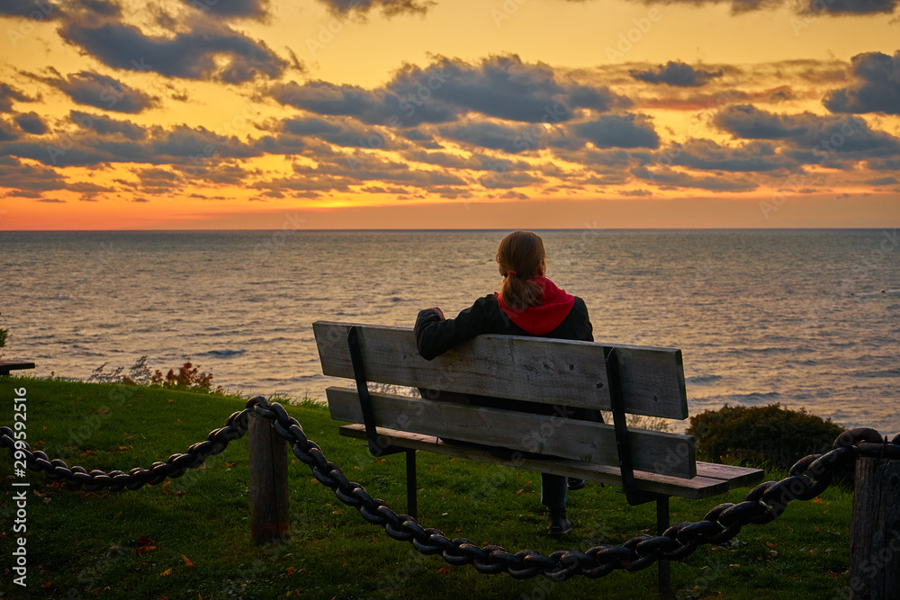 Woman sitting on bench at sunset over a lake