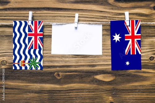 Hanging flags of British Indian Ocean Territory and Heard and Mcdonald Islands attached to rope with clothes pins with copy space on white note paper on wooden background. photo