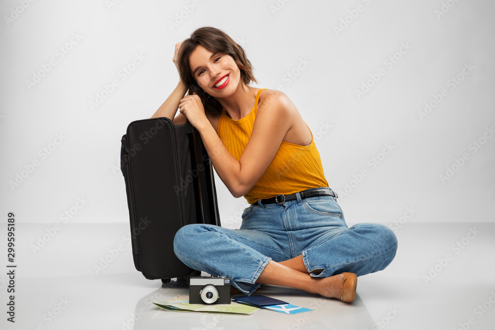 travel, tourism and vacation concept - happy smiling young woman in mustard yellow top with air ticket, camera, map and carry-on bag over grey background travel, tourism and vacation concept - happy smiling young woman in mustard yellow top with air ticket, camera, map and carry-on bag over grey background