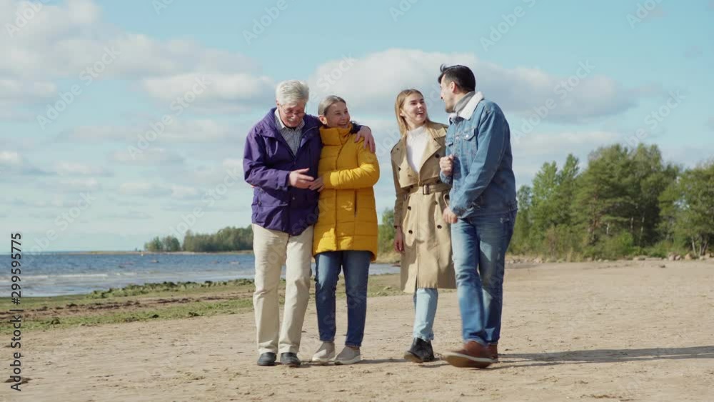 Two happy loving couples, senior and young lovers, walking on sea shore, talking joyfully and laughing on spring day. Young woman spending time with husband and parents Two happy loving couples, senior and young lovers, walking on sea shore, talking joyfully and laughing on spring day. Young woman spending time with husband and parents