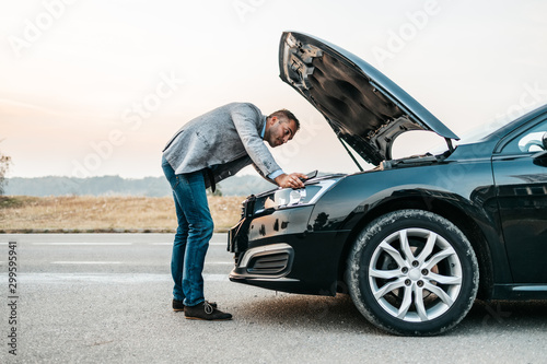 Elegant middle age business man trying to fix car breakdown or engine failure and waiting for towing service for help car accident on the road. Roadside assistance concept.