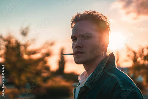 portrait of young man with 80s look smoking a cigarette during sunset