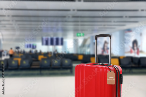 Red suitcase with TRAVEL INSURANCE label in airport terminal