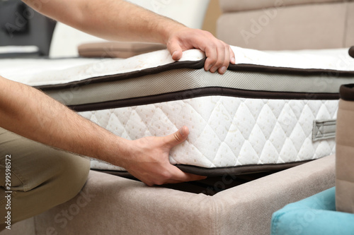 Young man choosing new orthopedic mattress in store, closeup photo