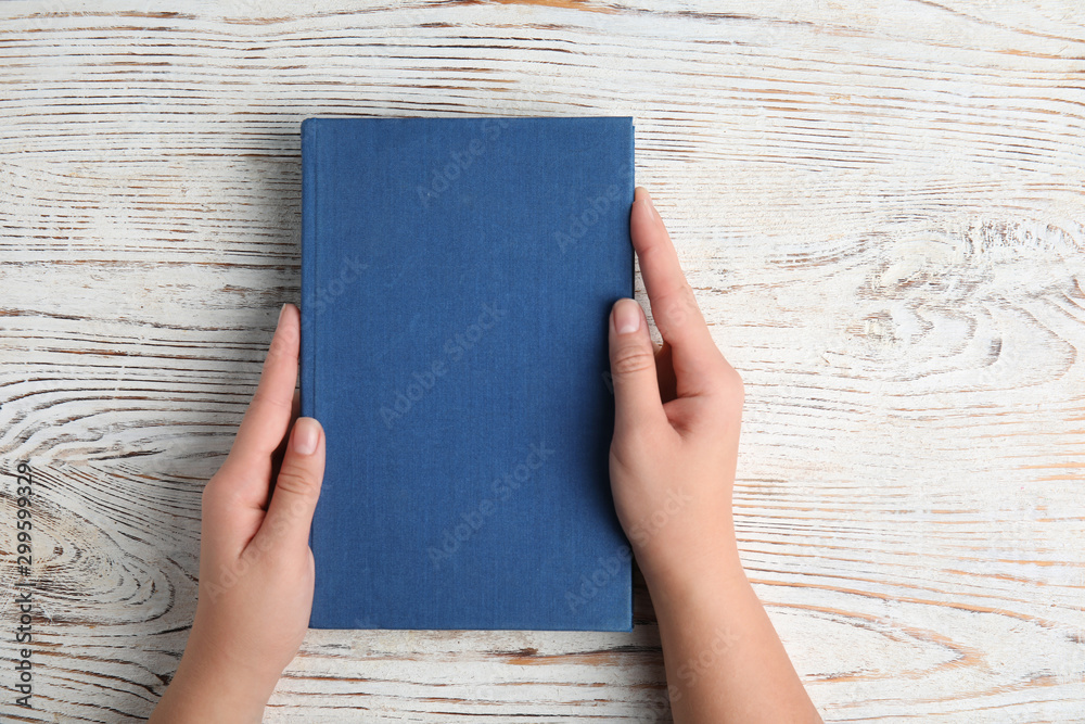 Woman holding hardcover book on white wooden background, top view Woman holding hardcover book on white wooden background, top view