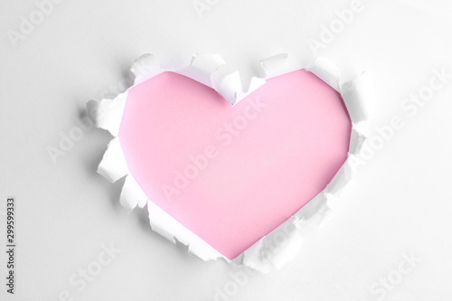 Torn heart shaped hole in white paper, top view. Pink space for text