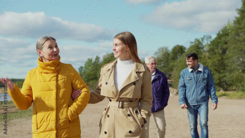 Medium shot of adult daughter talking with mother, while her husband talking with father behind. Two happy loving couples, senior and young lovers, on sea shore on spring day and having fun together Medium shot of adult daughter talking with mother, while her husband talking with father behind. Two happy loving couples, senior and young lovers, on sea shore on spring day and having fun together