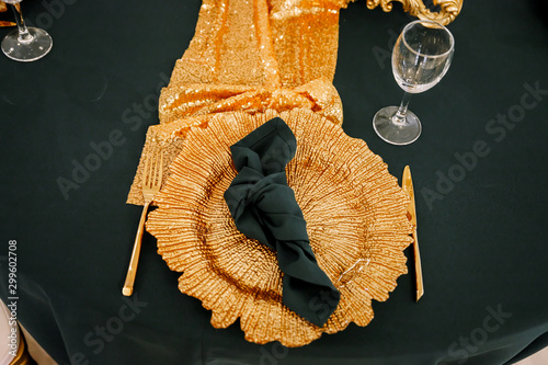 Table decoration with flowers in white colors. Elegant dining table in green-golden color. Indoors wedding. Devices and chairs in golden colors. Beautiful table setting, tablecloth green.