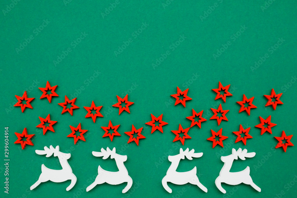 Wooden handmade Christmas decorations white Deers and red Stars with a pattern on a green isolated background. Flat lay, top view with copy space. Merry Christmas and Happy New Year concept.