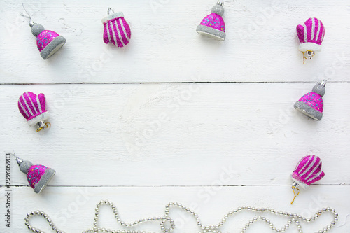Christmas background top view. Christmas decorations around the perimeter of pink and silver. New Year's toys in the form of hands and hats on a white wooden board background. New Year 2020