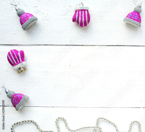 Christmas background top view. Christmas decorations around the perimeter of pink and silver. New Year's toys in the form of hands and hats on a white wooden board background. New Year 2020