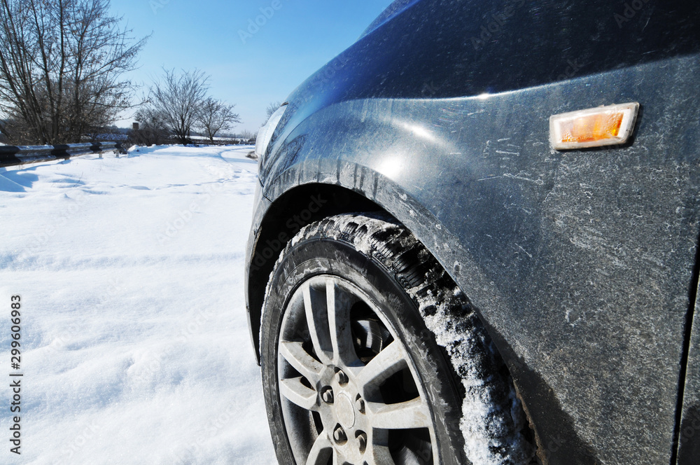 Close-up of a car on the snow near the road with trees against blue sky