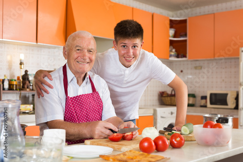 Cheerful teenage boy with grandfather in kitchen