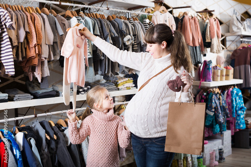 Pregnant woman and girl daughter choosing clothes