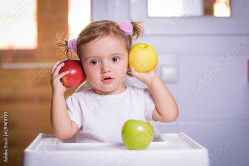Cute baby 1,4 years old sitting on high children chair and eating fruit alone in white and brown kitchen