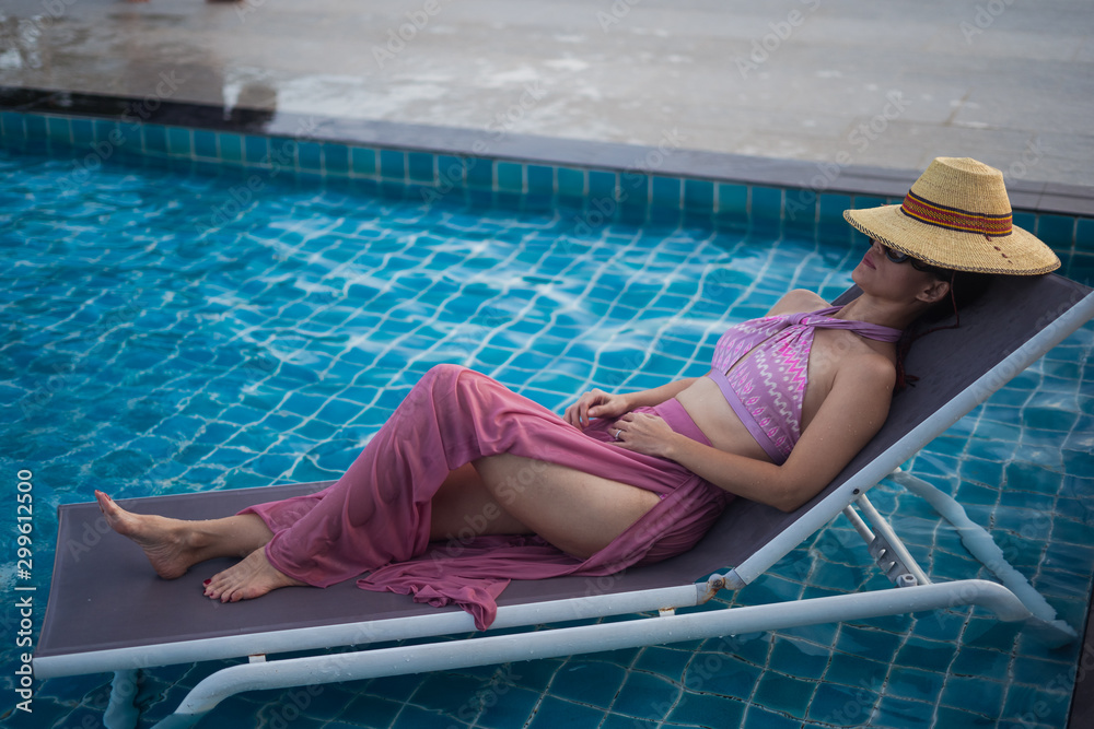 A woman wearing a swimsuit Wear sunglasses with straw hat Sitting on a  beach chair in the pool in the summer i Stock Photo | Adobe Stock