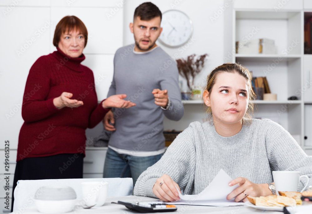 Obraz premium Distressed girl with paperwork and irritated family behind