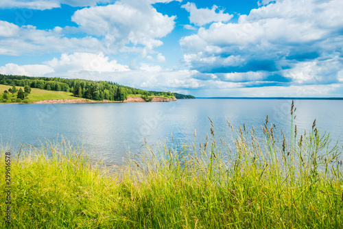 Beautiful panoramic view of the Kama river from the hill in the foreground green grass, summer blue sky with clouds.