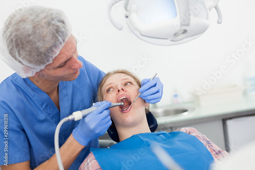 Male dentist treating young female patient in dental office