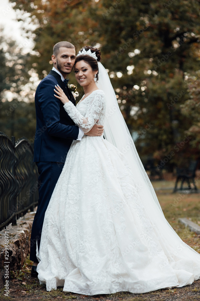 Wedding couple in autumn. Pretty bride and stylish groom.  Amazing smiling wedding couple. A nice bride and groom in a luxury dress look at each other in a fairy forest. Lovers and happy people