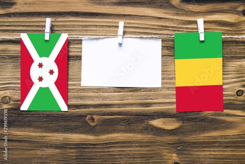 Hanging flags of Burundi and Mali attached to rope with clothes pins with copy space on white note paper on wooden background.Diplomatic relations between countries.