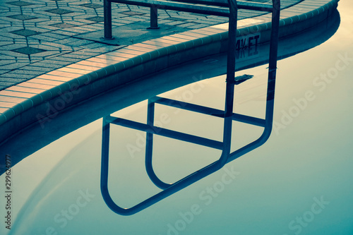 Abstract teal background with pool stairs railing reflected into a calm swimming pool.