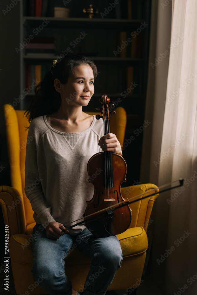 Beautiful young woman posing with a violin in her hand, sitting on a ...