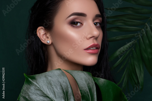 Brunette beautiful caucasian woman in flowers and leaves. Fresh, clean skin ccosmetology concept.
