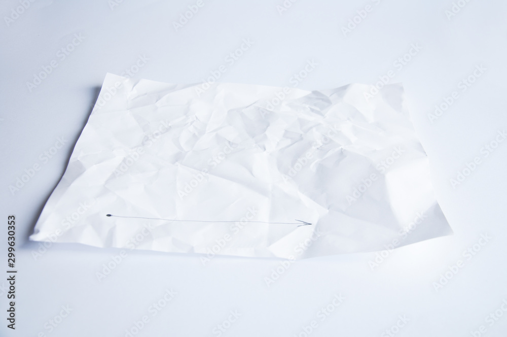 White crumpled sheet of paper lies on a table on a white background. On the sheet, a drawn line