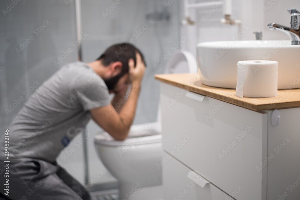 Hombre en el baño intentando vomitar en el inodoro