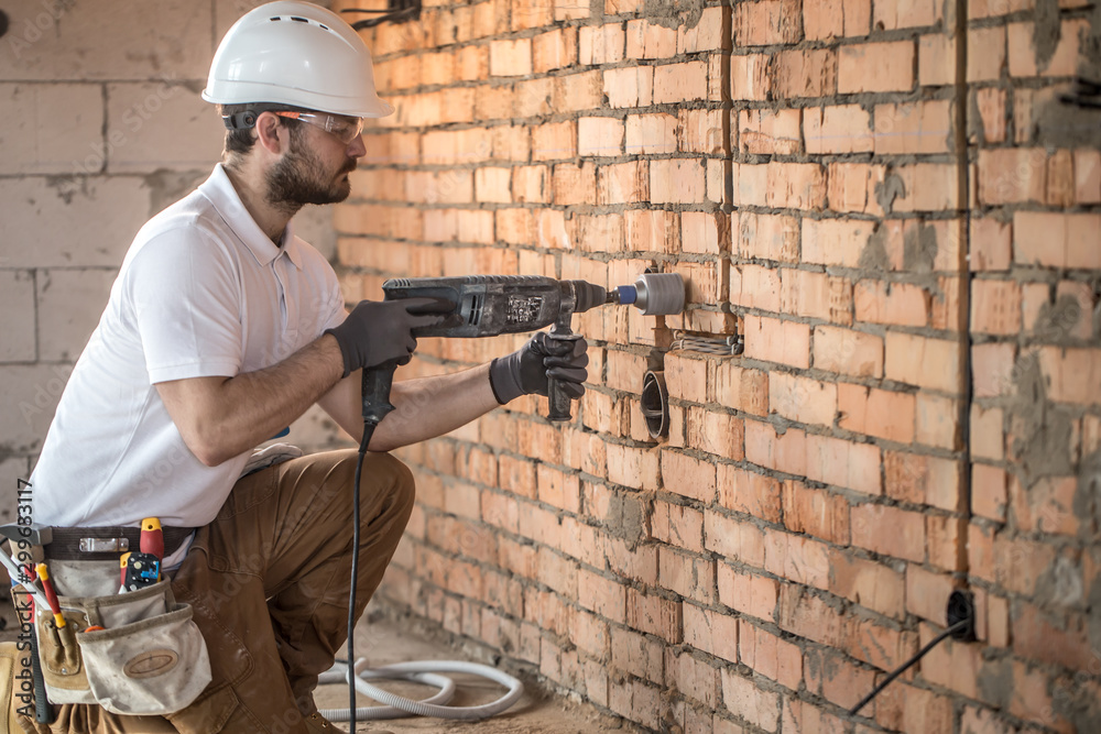 Handyman uses jackhammer, for installation, professional worker on the construction site. The concept of electrician and handyman.