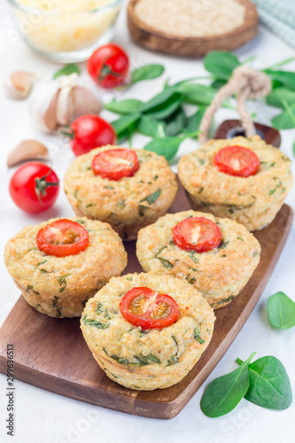 Savory muffins with quinoa, cheese and spinach topped with tomato, on wooden board, vertical
