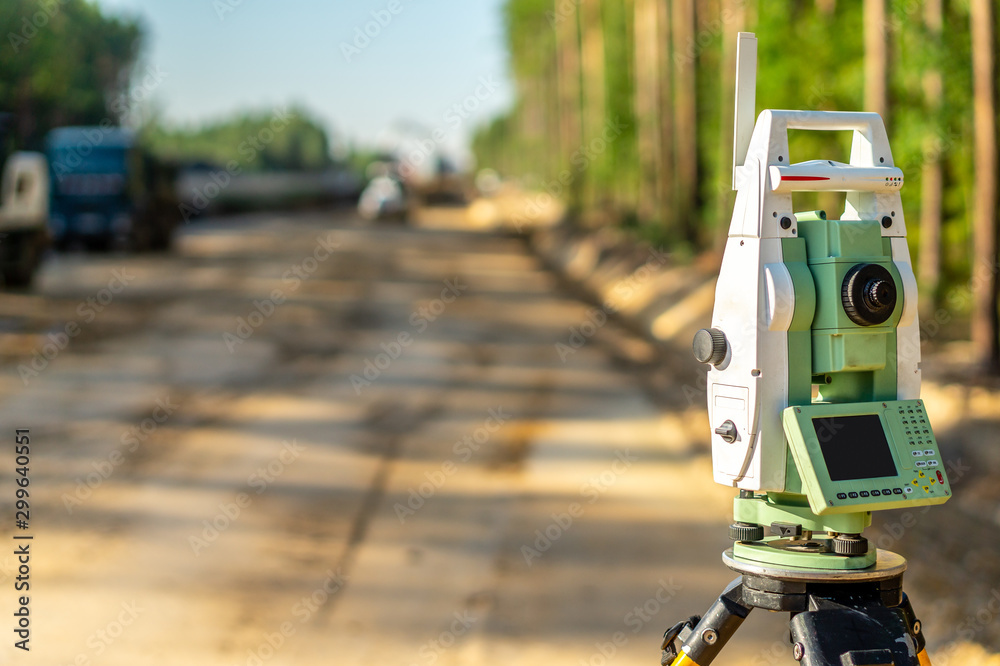 Surveyor engineer with equipment (theodolite or total positioning station) on the construction site of the road or building with construction machinery background Surveyor engineer with equipment (theodolite or total positioning station) on the construction site of the road or building with construction machinery background