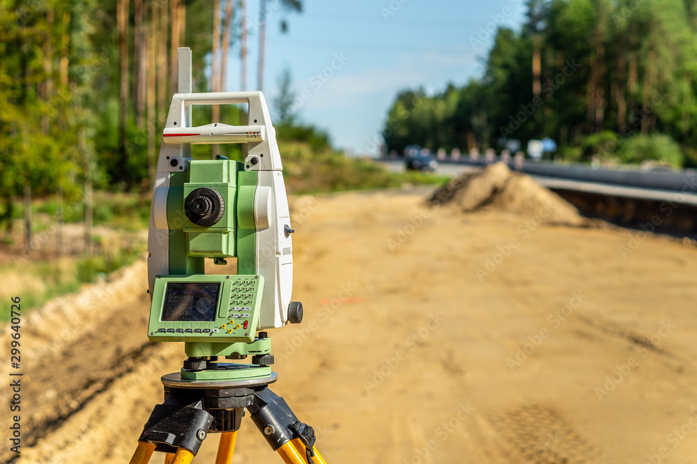 Surveyor engineer with equipment (theodolite or total positioning station) on the construction site of the road or building with construction machinery background