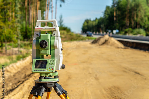 Surveyor engineer with equipment (theodolite or total positioning station) on the construction site of the road or building with construction machinery background