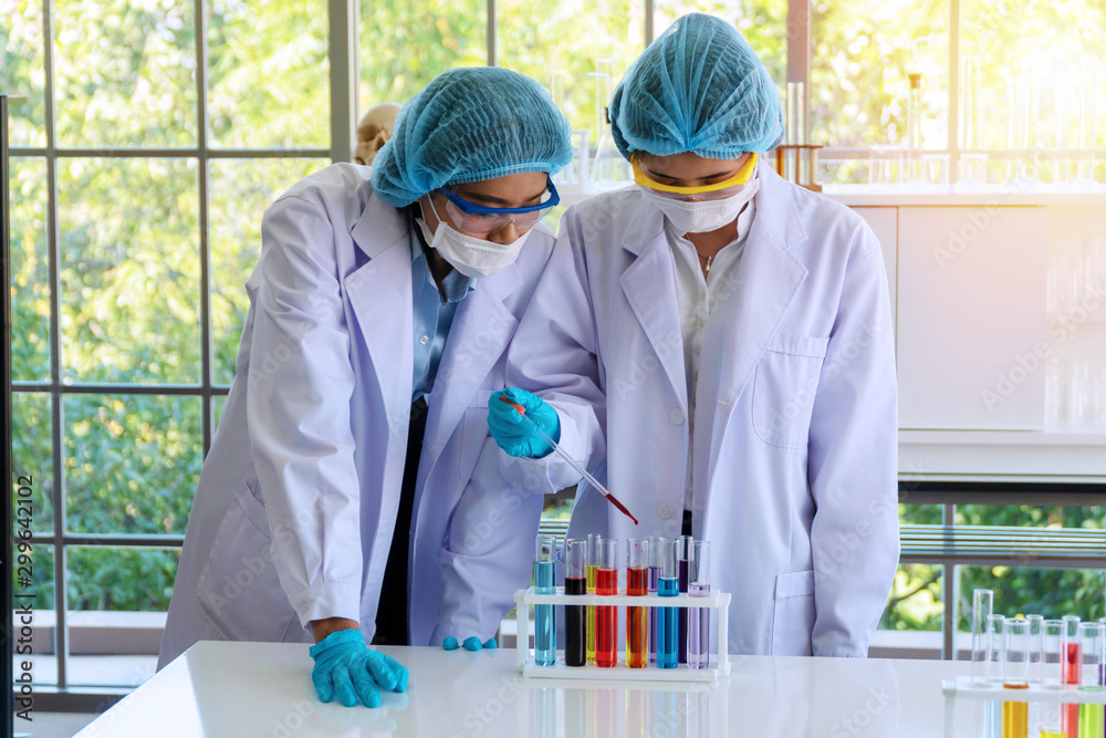 Group of chemistry working in the lab.Two young asian woman research scientist with wear lab coat,gloves and eyeglasses analyzing experiment together in laboratory, looking into tube. Science concept. Group of chemistry working in the lab.Two young asian woman research scientist with wear lab coat,gloves and eyeglasses analyzing experiment together in laboratory, looking into tube. Science concept.