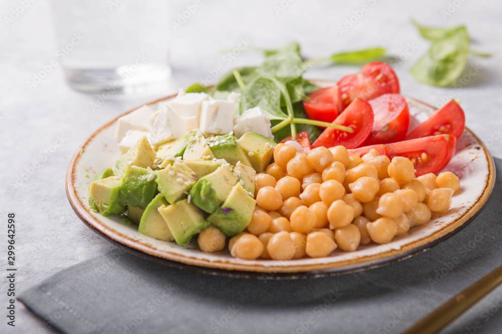 Buddha Bowl with Avocado, chickpea, feta cheese, fresh spinach, Tomatoes and glass of water. Concept for healthy vegetarian detox balanced meal. Top view. Copy space.