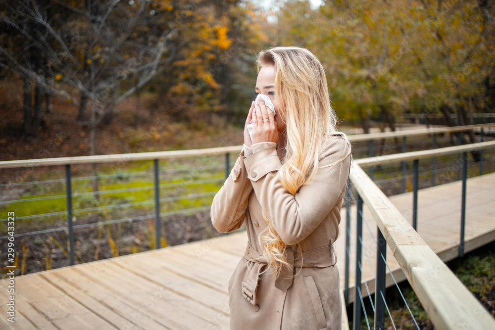 Young european woman blowing her nose with a tissue. Seasonal allergies. Cold and flu in autumn. Young european woman blowing her nose with a tissue. Seasonal allergies. Cold and flu in autumn.