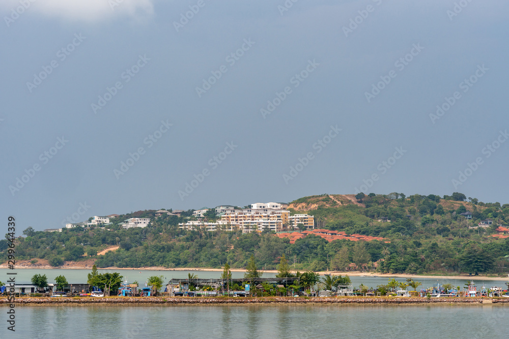 Ko Samui Island, Thailand - March 18, 2019: Looking northeast from Wat Phra Yai Buddhist Temple on Ko Phan. Dam pier in front and hills with white and red roofed villas in tourist resorts under blue s