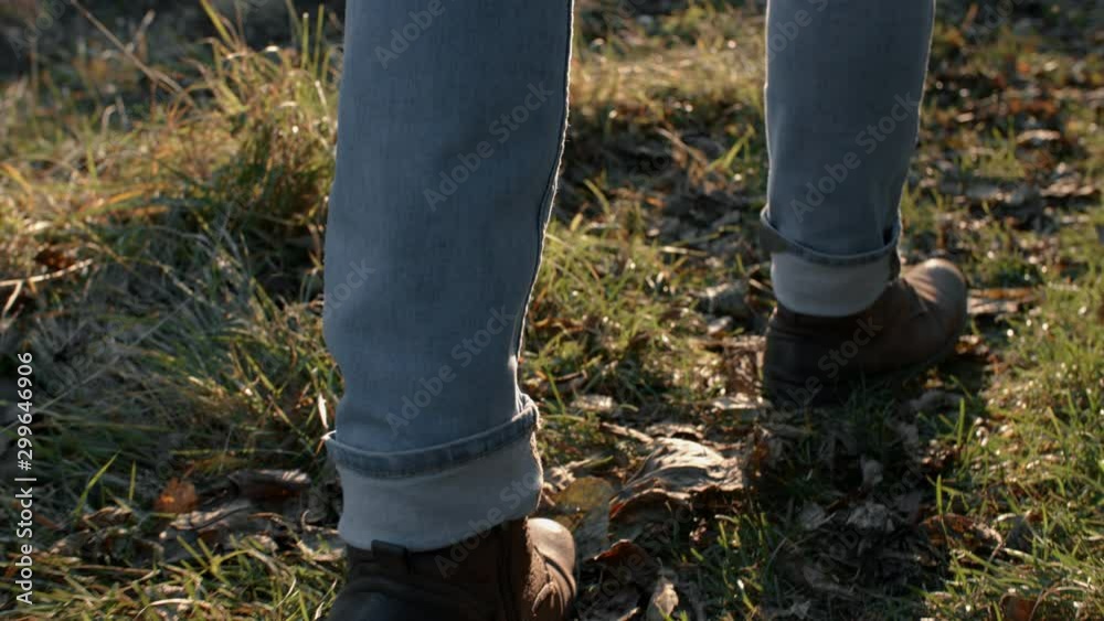 Close-up man legs/feet steep terrain on field in evening rays of sun, steadicam shot. Male hiker traveler in jeans and boots making steps, hiking, autumn season trekking, stepping on fallen leaves Close-up man legs/feet steep terrain on field in evening rays of sun, steadicam shot. Male hiker traveler in jeans and boots making steps, hiking, autumn season trekking, stepping on fallen leaves