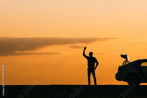 The male driver raised his hand and is waiting for help  his car cannot move further after a breakdown at sunset  side view  copy space. Votes on road concept.