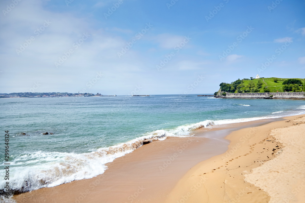 Landscape with a sandy beach and embankment of Saint-Jean-de-Luz, green hill with white chapel on top (Basque Country, Atlantic coast, France). Coastal french town at sunny summer day. Sea shore