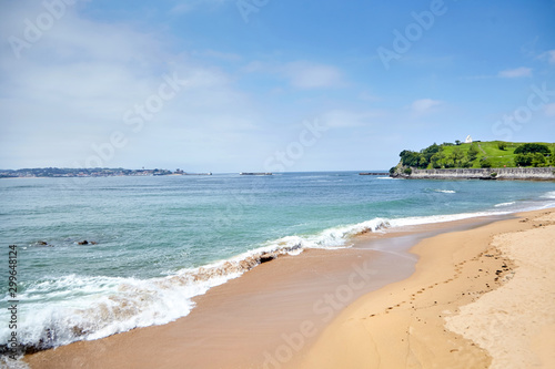 Landscape with a sandy beach and embankment of Saint-Jean-de-Luz, green hill with white chapel on top (Basque Country, Atlantic coast, France). Coastal french town at sunny summer day. Sea shore